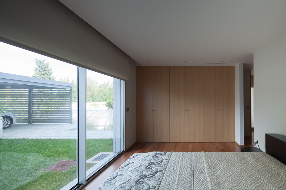 这是一间卧室，在玻璃门对面有一张巨大的深色木质平台床，通向室外区域，为硬木地板带来自然光。