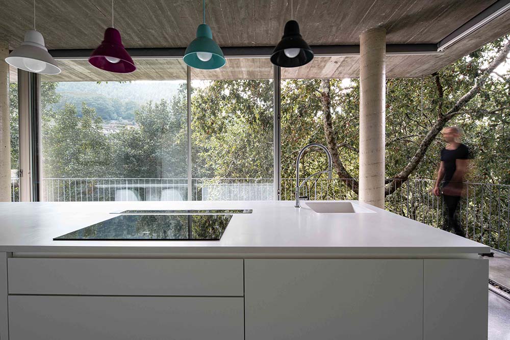 厨房岛的白色现代橱柜和柜台被从玻璃墙射入的自然光照亮。