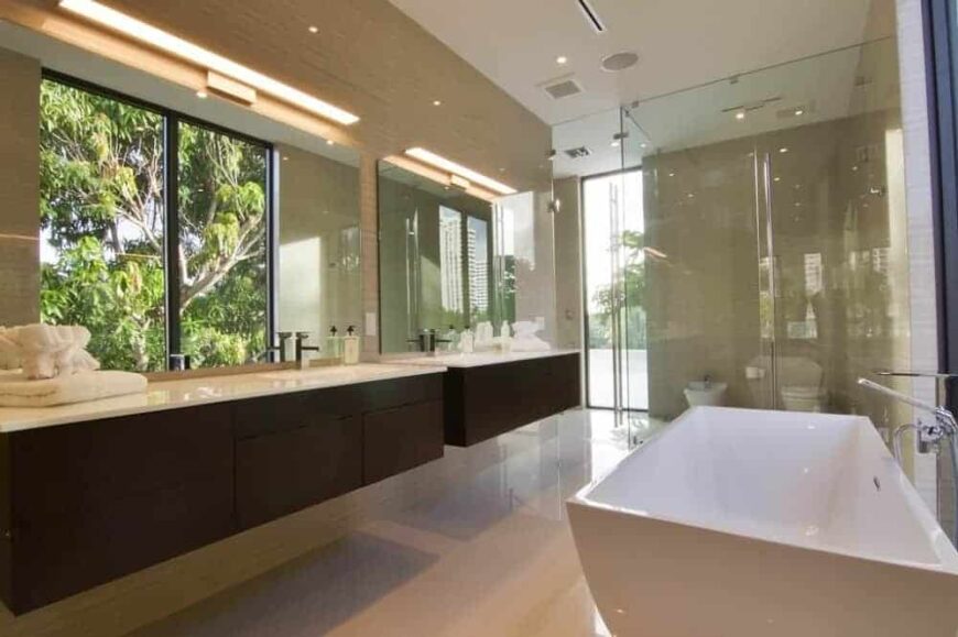 主浴室里有一个浴缸，对面是带有两个水槽的浮动梳妆台，梳妆台的深棕色与米黄色的地板和墙壁形成对比。
