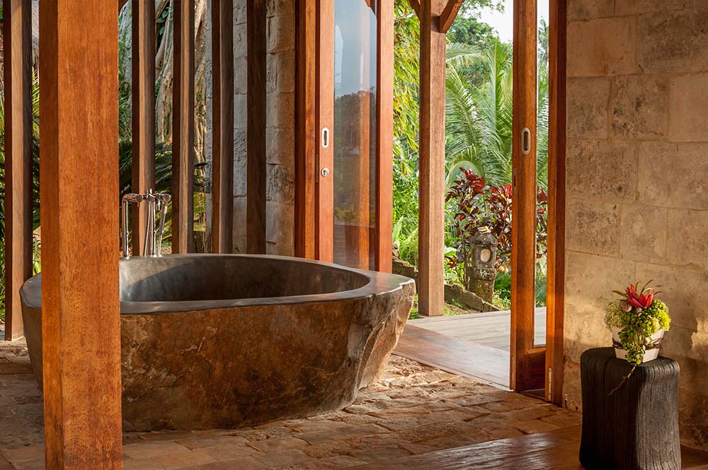 浴室里有一个质朴的石头浴缸，外面是有质感的深棕色色调，周围是木柱。