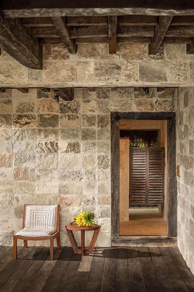 房子的这个角落的墙壁上有纹理的石块，与木制软垫椅和顶部有外露横梁的木制边桌相辅相成。