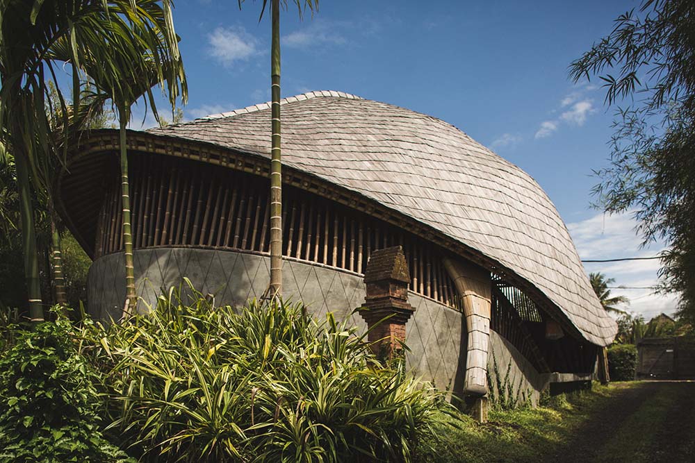 这是房子的侧面，有混凝土基础墙，竹格栅，顶部有一个由热带树叶编织而成的大碗状屋顶。