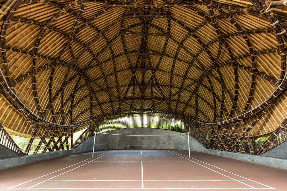 这是一个有顶棚的大型排球场的内部景观，天花板上有裸露的竹梁。
