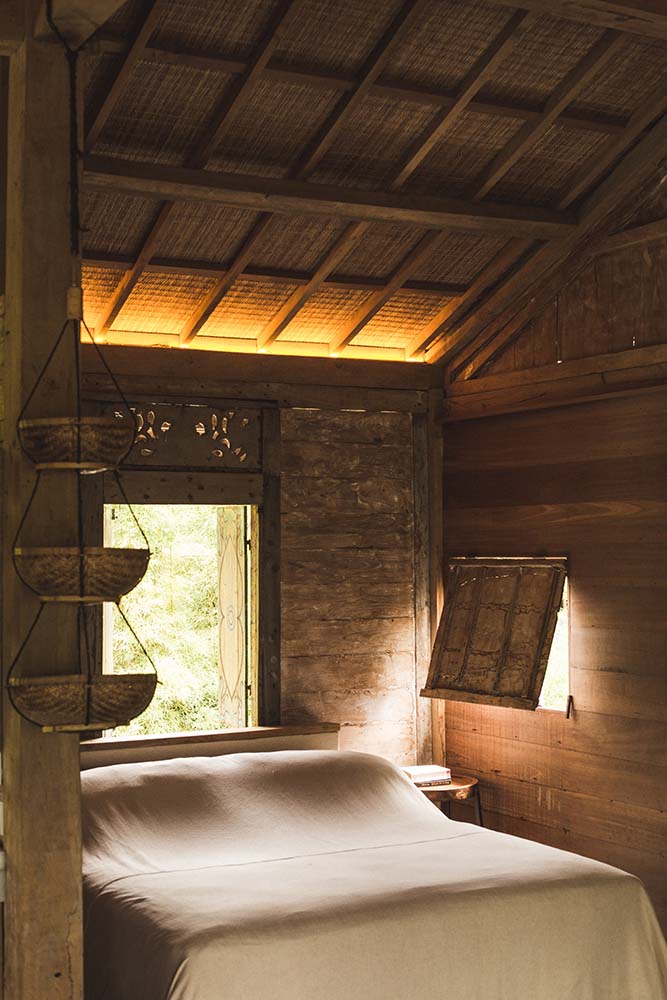 这是客房的卧室，有一张简单的床，周围是质朴的木墙，顶部是高高的木制天花板。