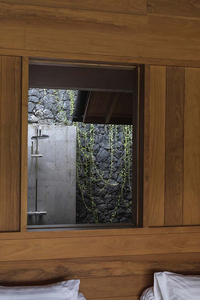这是床床头板上方的一扇木窗，可以看到带有马赛克纹理石墙和蔓生藤蔓的淋浴区。