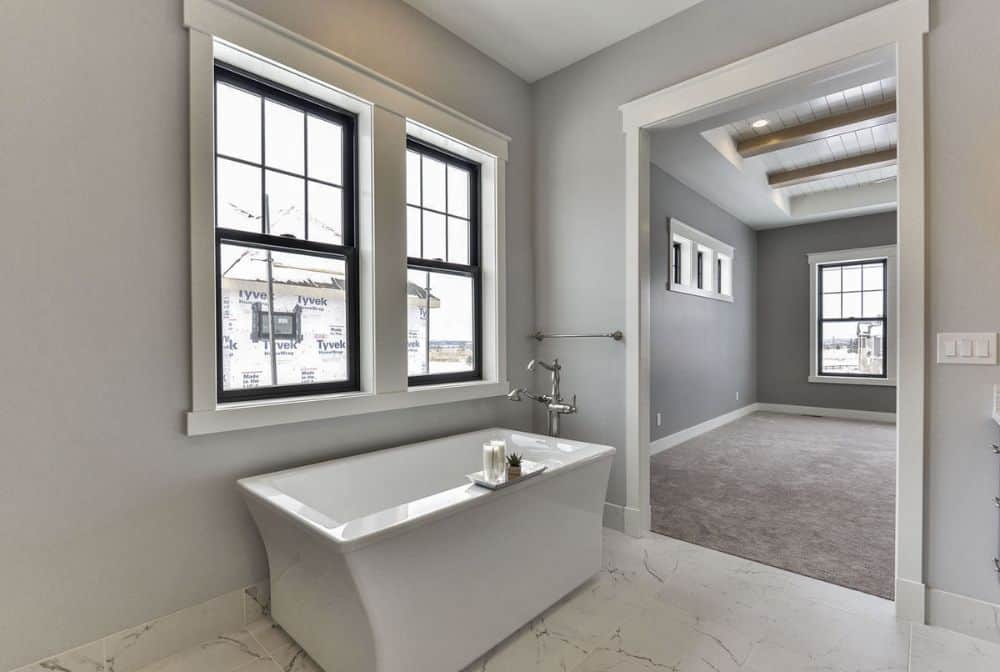 大理石瓷砖地板上的独立式浴缸位于框架窗的下方。