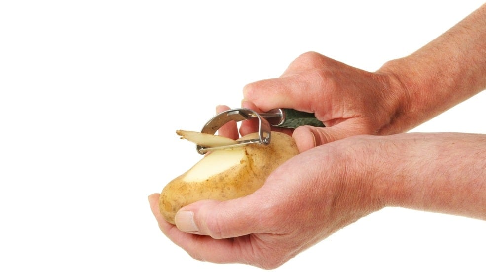 一双用快速削皮机削土豆的手。