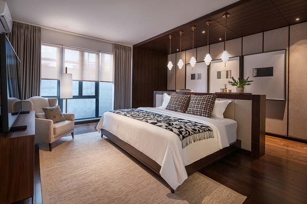 主卧室有一张深色木制的大床，与带有深色木制元素的凹室相匹配，辅以一排吊灯和壁挂式艺术品。