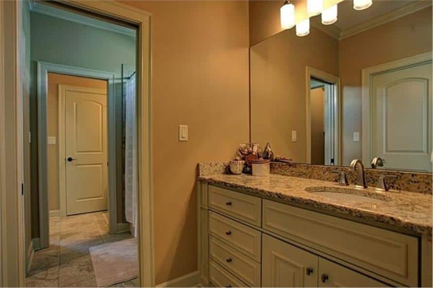 浴室里有一个白色的梳妆台，上面有一个瓷水槽，花岗岩台面，和一面无框镜子。