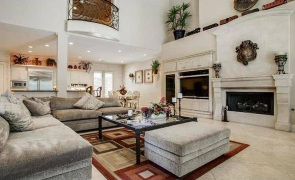 家庭娱乐室提供天鹅绒座椅、带图案的区域地毯、玻璃桌和大理石壁炉。