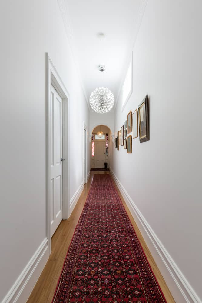 这是一条长长的走廊，有白色的墙壁和硬木地板，上面铺着红色图案的地毯。