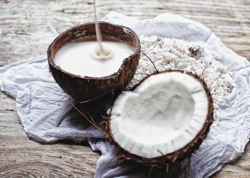 成熟的椰子裂成两半，与椰子肉、椰奶和干椰子放在一块布上，放在木桌上