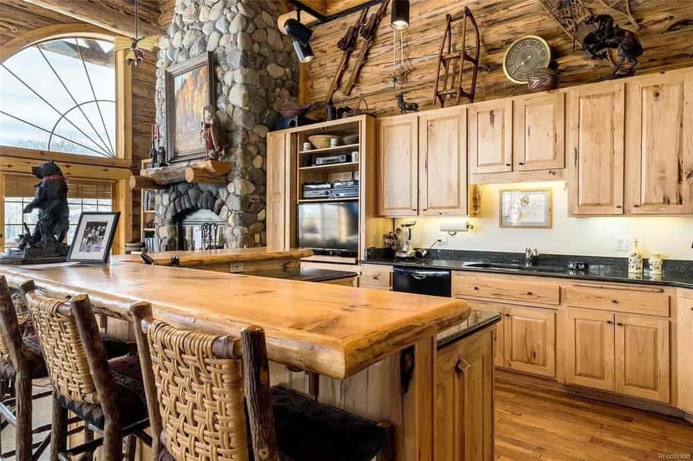 这是一个带有木制橱柜的乡村厨房，与硬木地板和木梁墙的色调相匹配。这是搭配一个l形的厨房岛，有一个早餐吧。