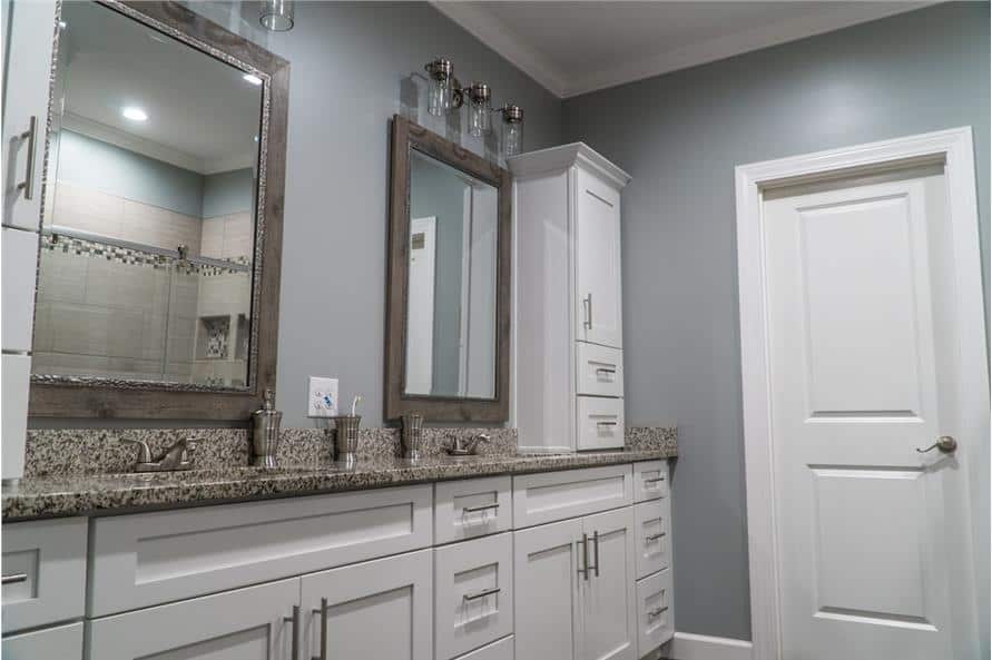主浴室有一个双洗手池梳妆台，上面有一个白色橱柜和几面木框镜子。