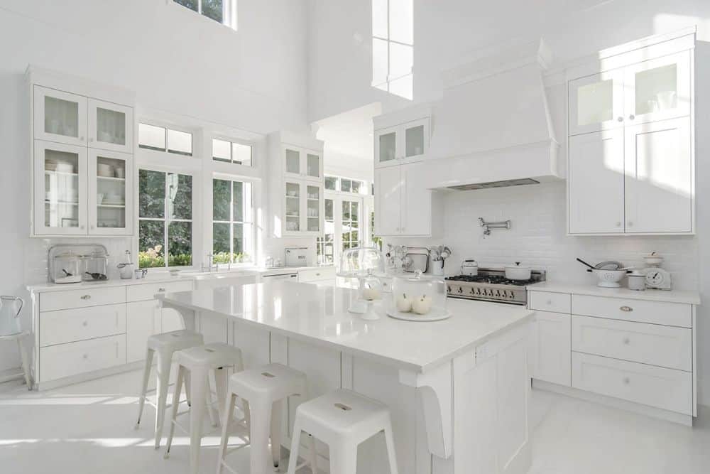 厨房用白色和座造价橱柜,不锈钢炉灶,地铁瓷砖连壁,早餐酒吧内衬白色的酒吧凳。