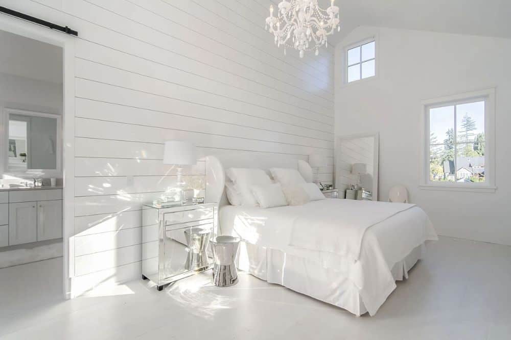 主卧室带有白色搭叠口音墙,白色的家具,一个拱形的天花板上安装的串珠吊灯。