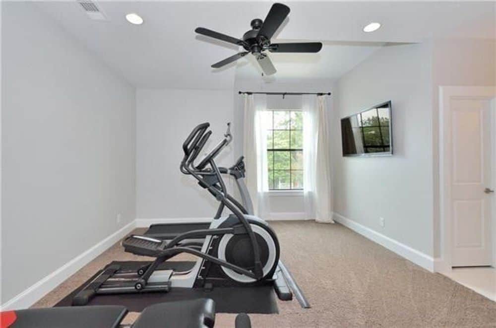 家庭健身房，有壁挂式电视和地毯地板上的健身器材。