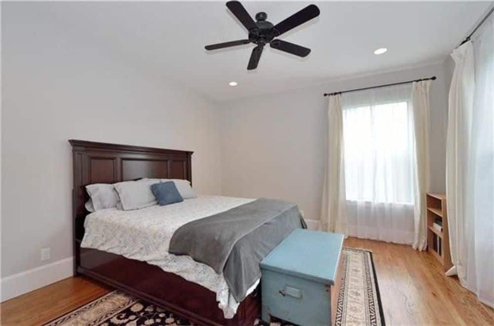 这间卧室里有一张深色的木床，储物凳，硬木地板上铺着带边框的地毯。
