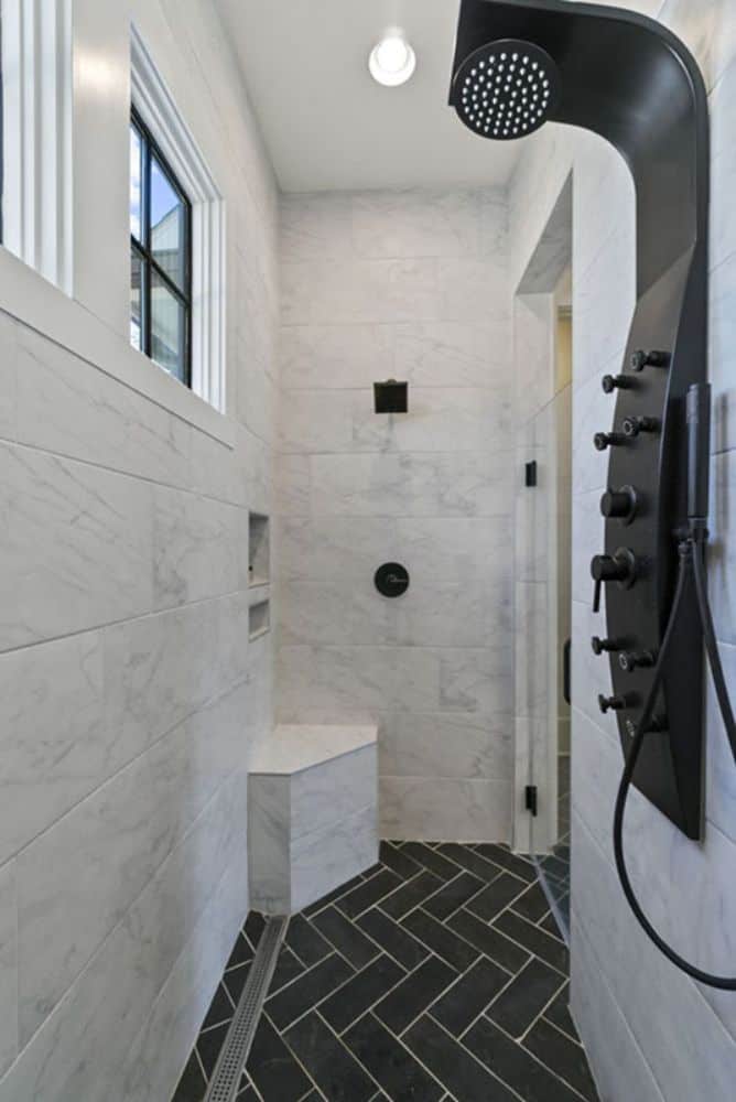 步入式淋浴间有大理石瓷砖墙壁，角落里有一个座位，以及哑光黑色的固定装置。