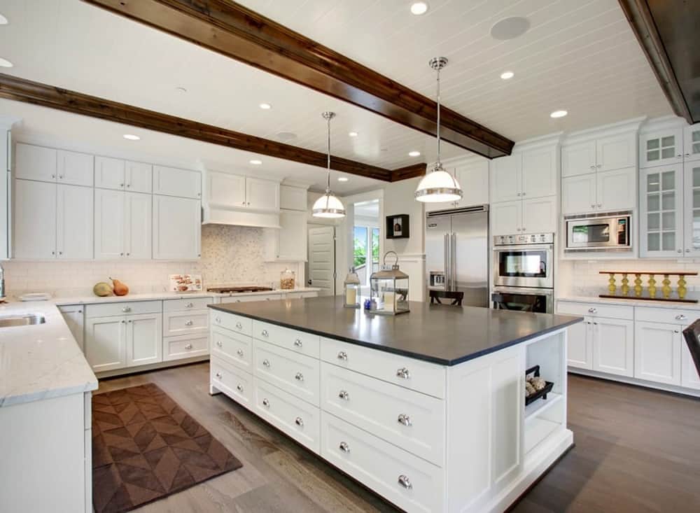 厨房主要由墙壁上的纯白色摇壶柜和大厨房岛台上的配套摇壶抽屉组成，与它的黑色柜台形成对比。然后，米色的后挡板和暴露的天花板木梁补充了这些。