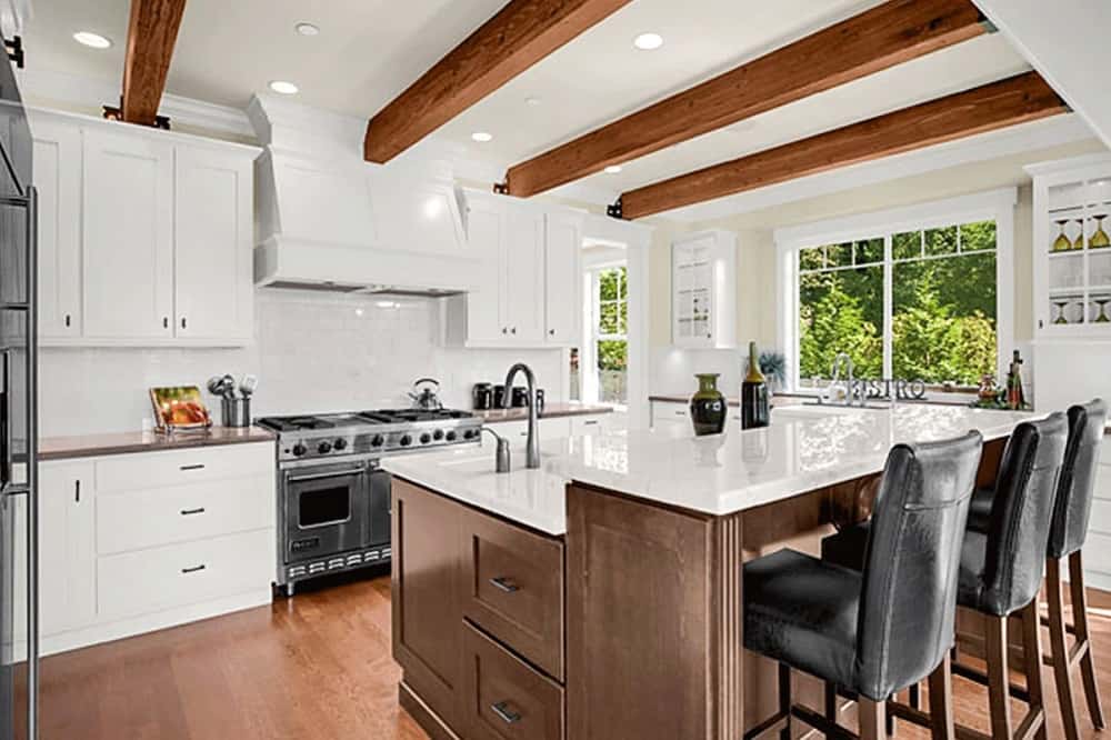 这是一个近距离观察厨房与一个大的两层厨房岛。这里有一个白色的台面，与之形成对比的是棕色的木制橱柜，与硬木地板和裸露的天花板横梁相匹配。
