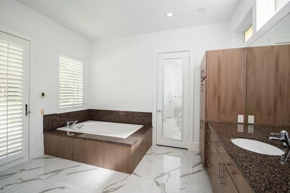 浴室有洗手台，亚麻衣柜，大理石瓷砖地板上有一个可入式浴缸。