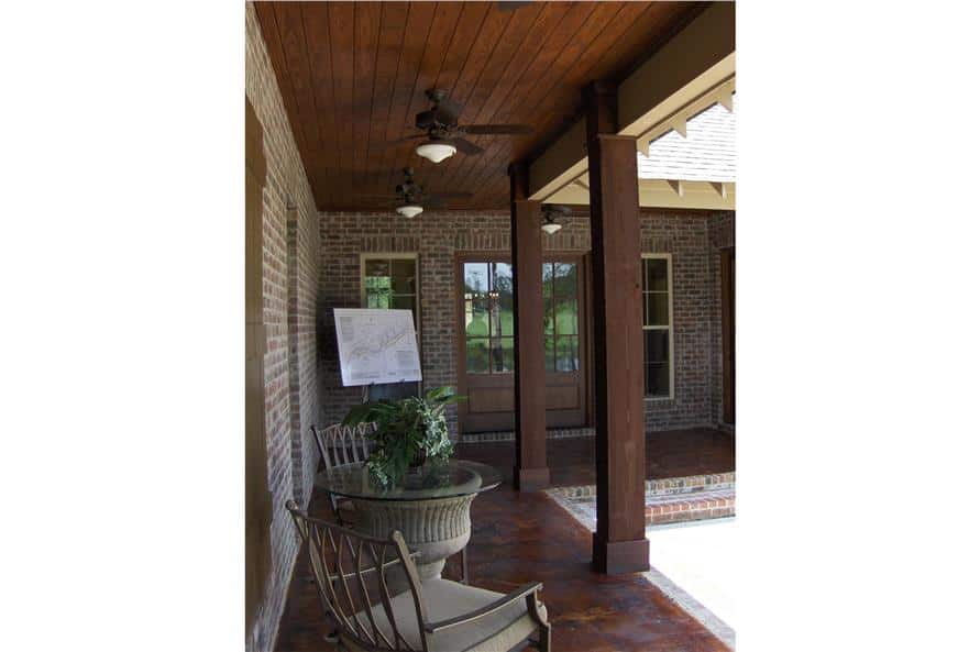 带顶棚的门廊里有带软垫的扶手椅、一张玻璃顶边桌，以及安装在木板天花板上的吊扇。