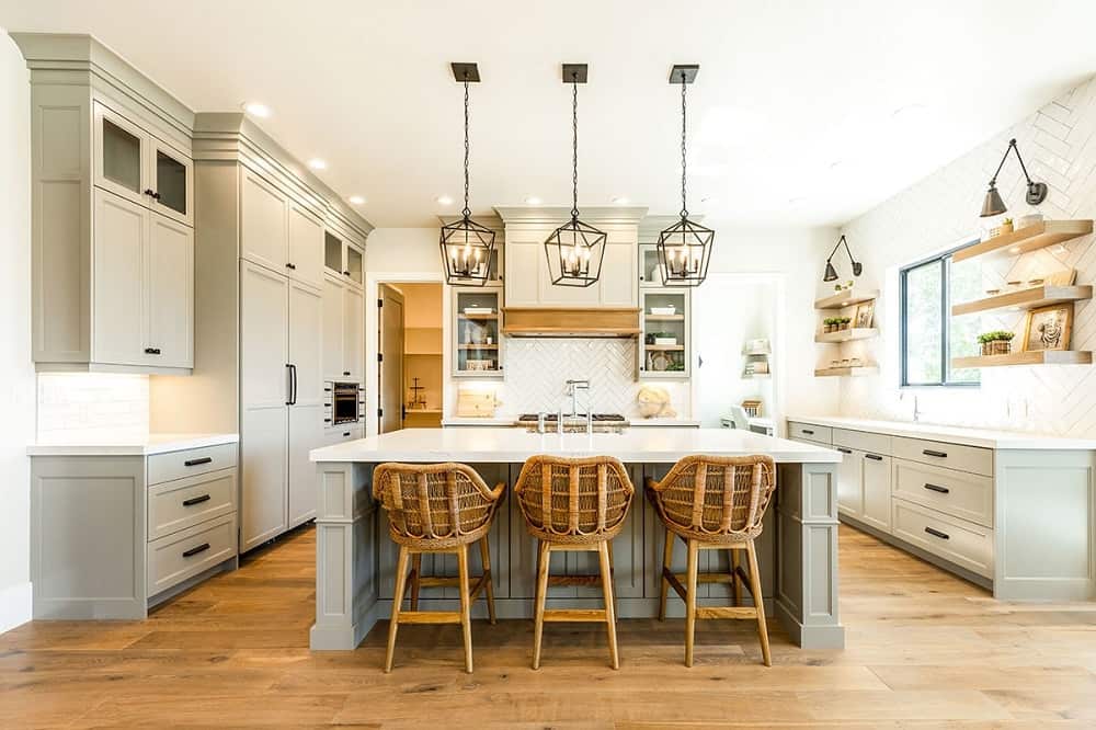 这是一个大厨房的近景，灰色的橱柜与灰色的厨房岛台相匹配，白色的天花板上挂着三盏吊灯。这是搭配编织柳条凳早餐吧。
