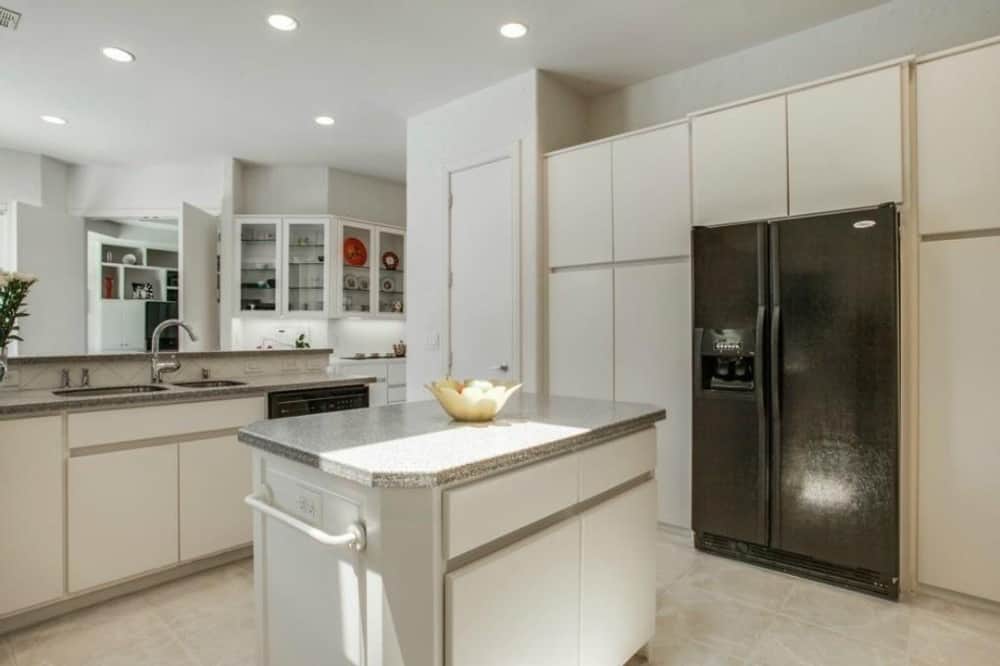 厨房的特点是白色橱柜、黑色电器、一个中心岛台和一个配有双碗水槽和一个凸起的餐吧的半岛。