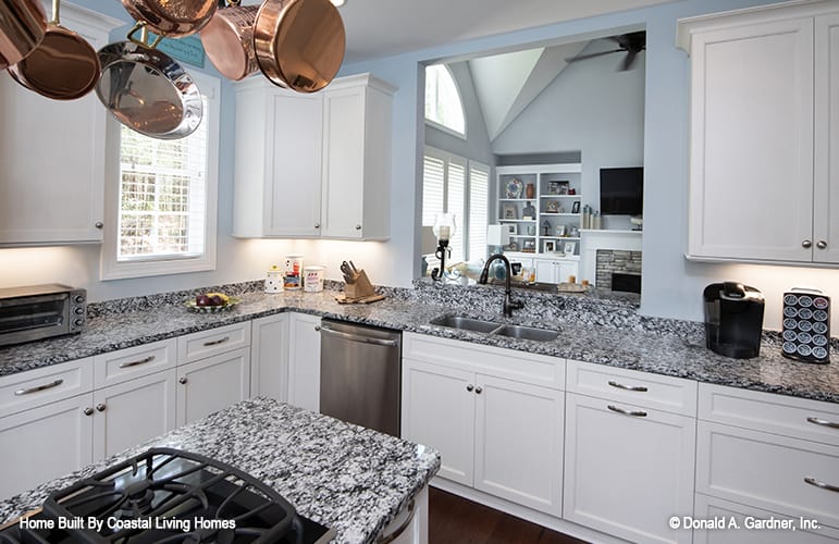 厨房配备了一个双碗水槽、花岗岩台面、白色橱柜和一个悬挂在灶台岛上的锅架。