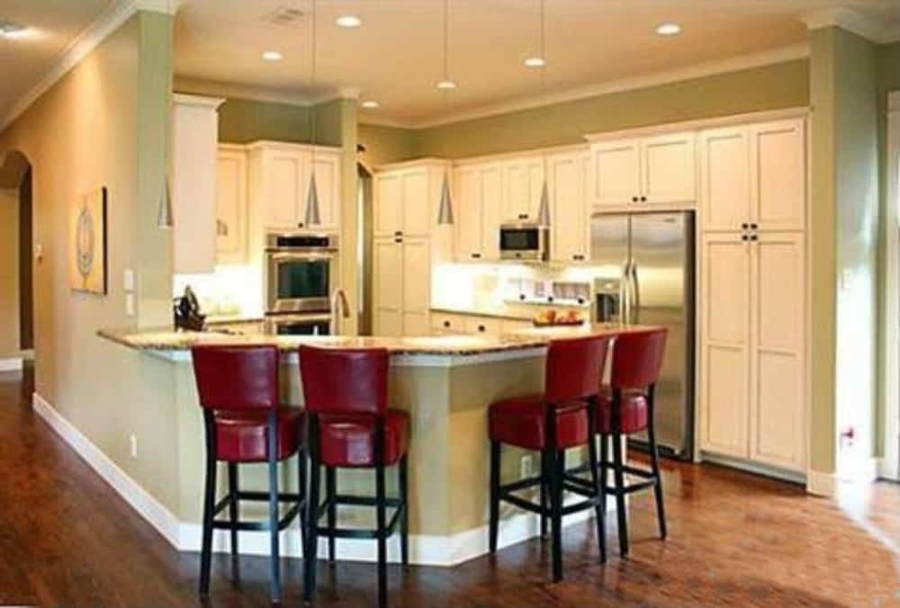 厨房里有白色橱柜，不锈钢用具，弯曲的用餐吧台，搭配红色皮革柜台椅。