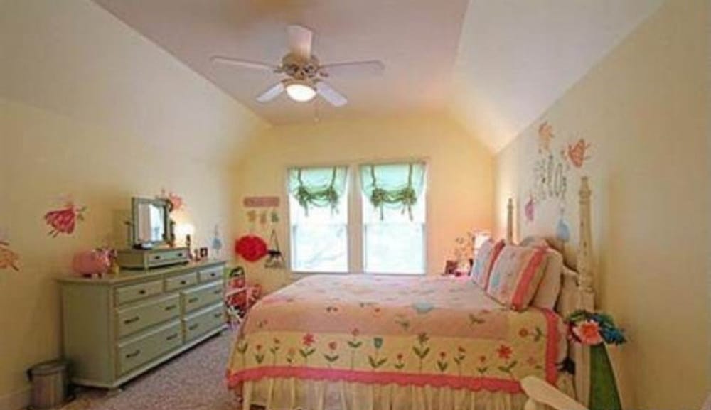 卧室有凹形天花板，一张破旧的白色床，地毯地板上有一个薄荷绿色的梳妆台。