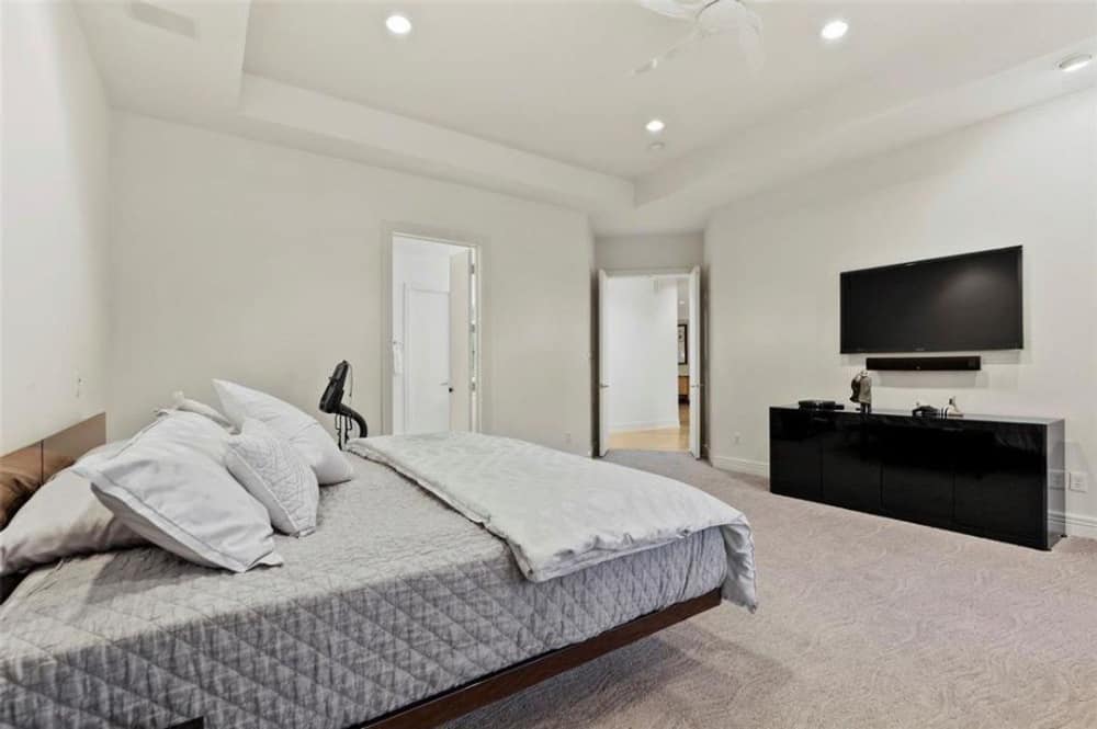 另一间卧室有托盘天花板，地毯地板，一张厚底床和壁挂式电视。