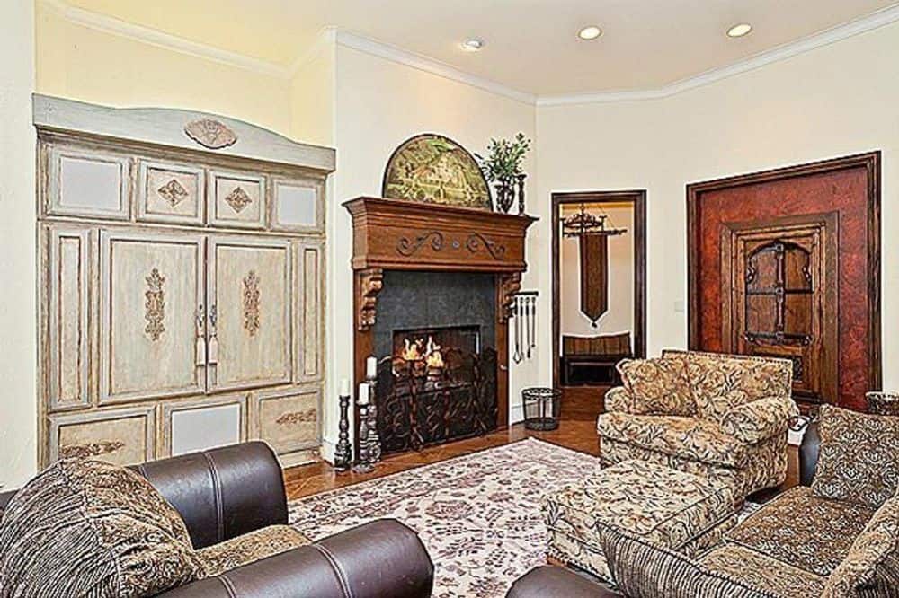 家庭娱乐室里有带图案的座椅，浅色木质嵌壁式家具，以及一座带木制壁炉架和锻铁屏风的壁炉。