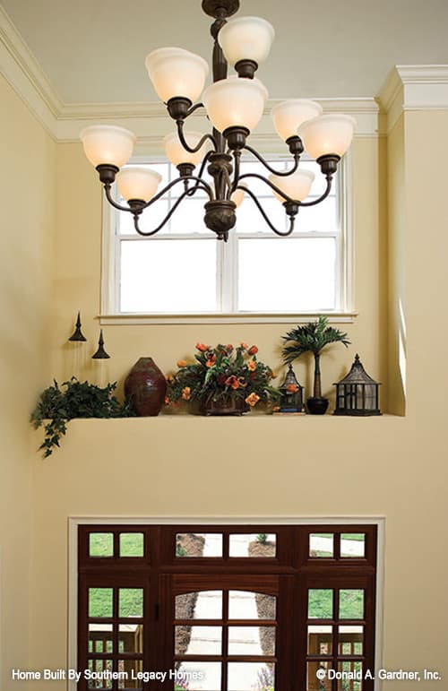 门厅，米色墙壁，一扇玻璃门，两层高的天花板上挂着一盏锻铁枝形吊灯。