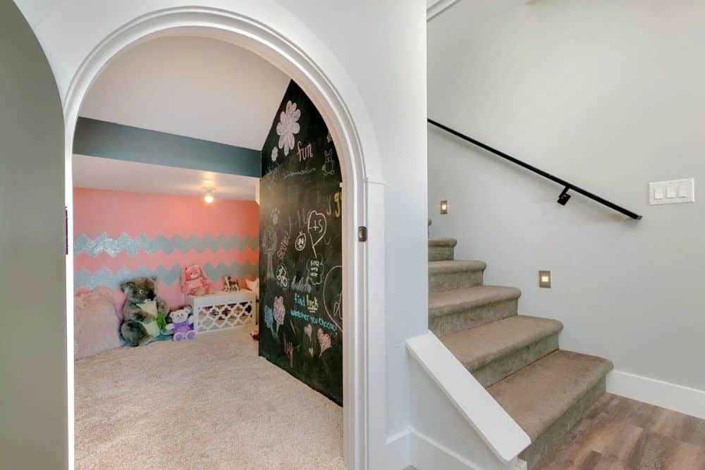 一扇拱形门通往儿童游戏室，里面铺着地毯和黑板墙。