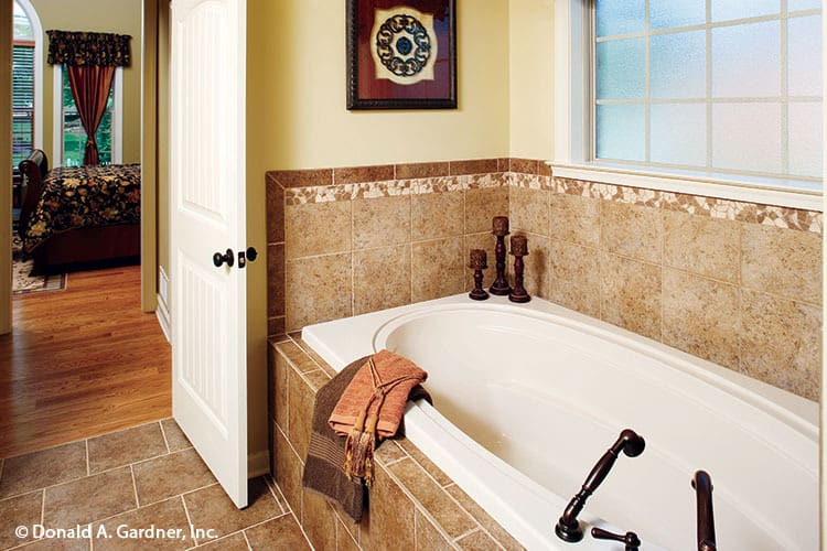 主浴室带一个深浴缸，配有锻铁固定装置和瓷砖后挡板和环绕。