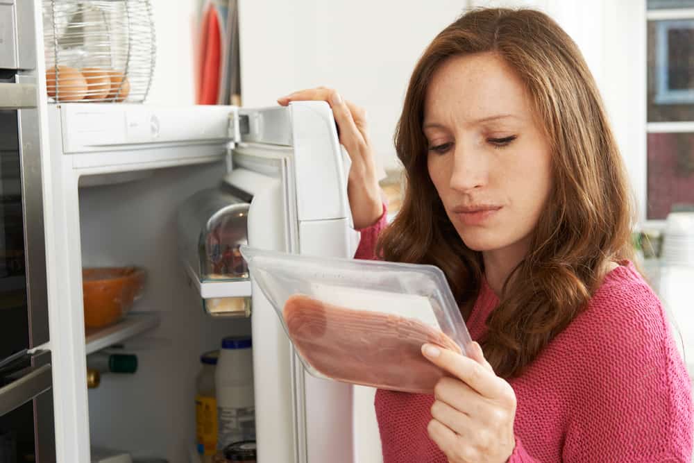一个女人从冰箱检查包装火腿。