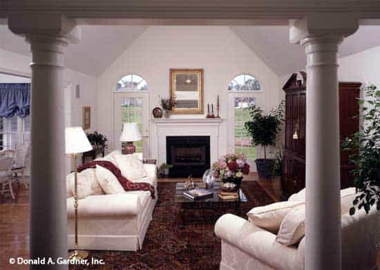 大房间里有圆形柱子，大教堂天花板，玻璃围成的壁炉，带裙边的沙发搭配深色的木头咖啡桌。