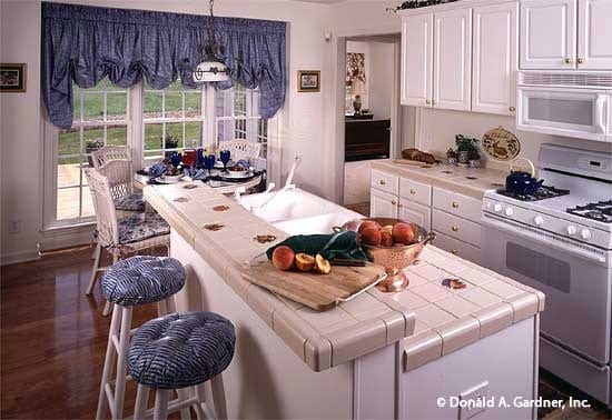 厨房提供白色橱柜和电器，一个双碗水槽，和一个带簇状圆形凳子的早餐岛。