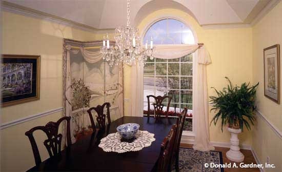 正式的餐厅有一个拱形的天花板，一个长方形的餐厅，植物底座，黄色的墙壁上装饰着装裱好的艺术品。