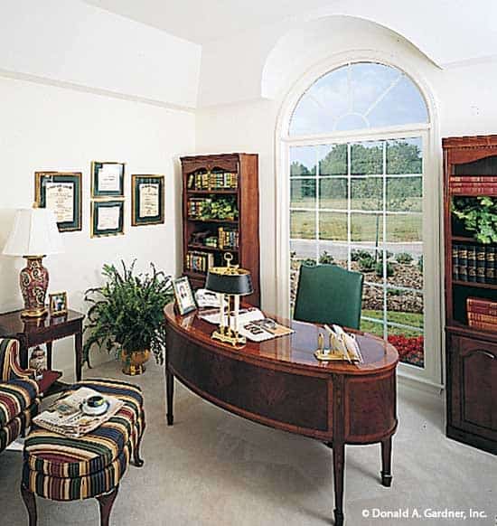 书房有木制书柜，椭圆形的桌子，条纹躺椅，和一个大窗户俯瞰宁静的周围。