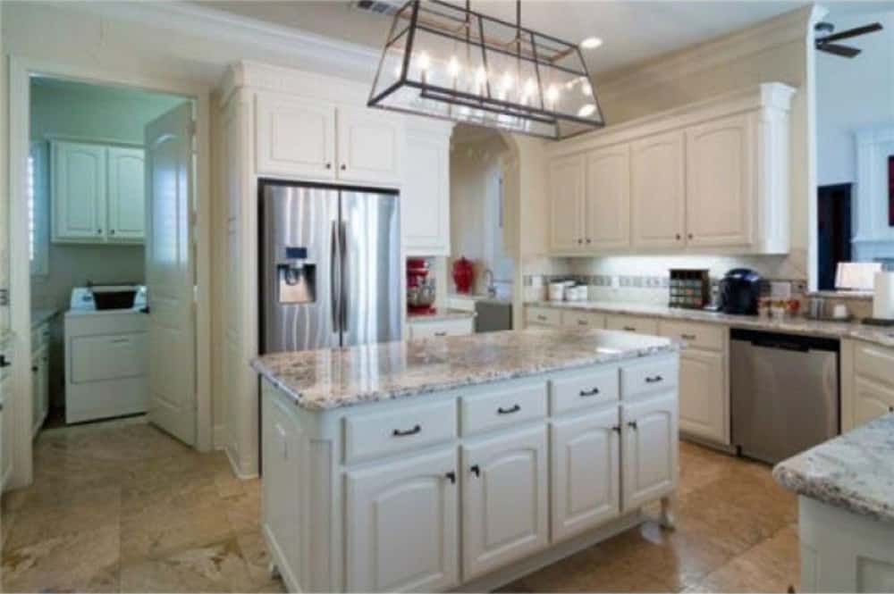厨房提供白色橱柜，不锈钢电器，和一个由线性吊坠照明的中心岛。