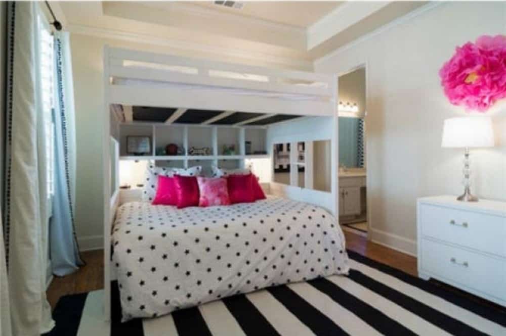 这间卧室有嵌壁式书架、白色家具，硬木地板上铺着条纹地毯。