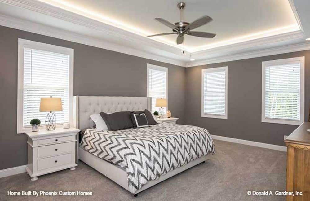主卧室的特点是一张簇绒床，灰色墙壁和一个装有铬风扇的托盘天花板。