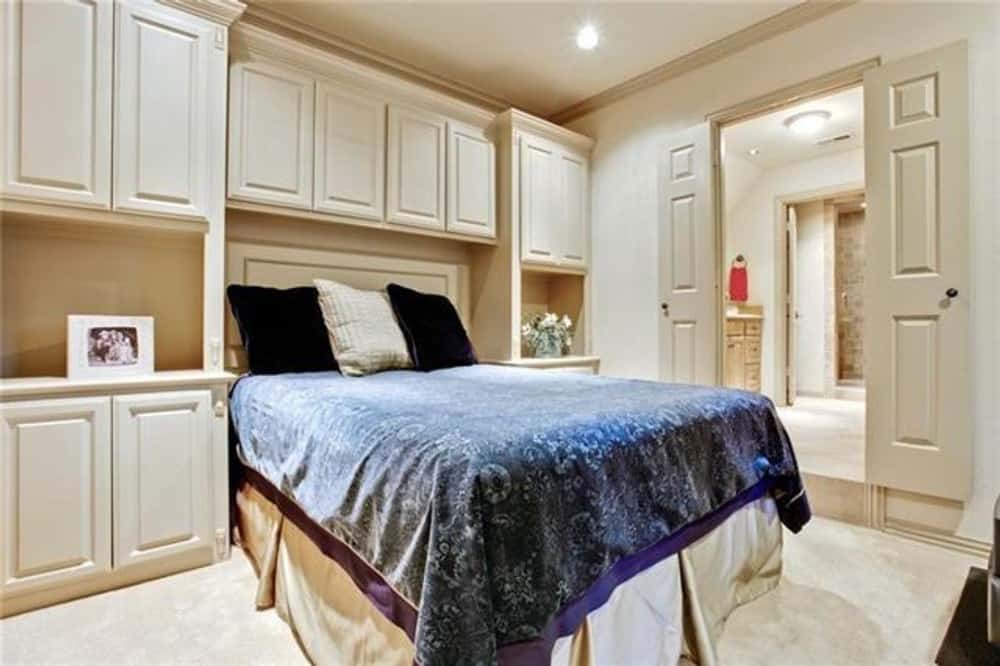 主卧室里有白色的嵌壁式家具，地毯地板上有一张有裙边的床。一侧有一扇双开门，通往主浴室。
