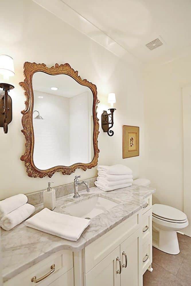 这间浴室设有一间厕所和一个大理石梳妆台，上面装饰着一面装饰性的镜子和烛台。