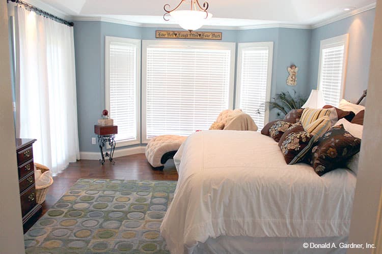 主卧室有蓝色的墙壁，大窗户，硬木地板，上面有图案的区域地毯。