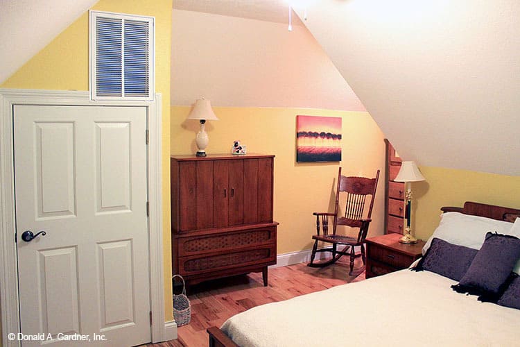 这间卧室有拱形天花板，木制家具，黄色的墙壁上装饰着一幅画。