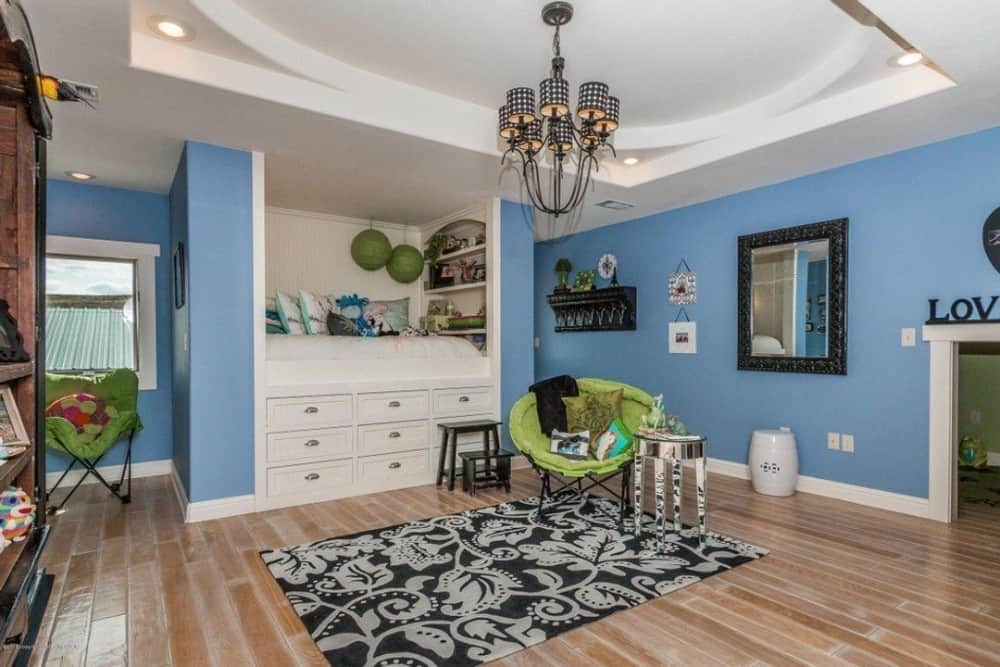 这间卧室有蓝色的墙壁、硬木地板、绿色的座椅和一张嵌壁式沙发床，床下有储物空间。